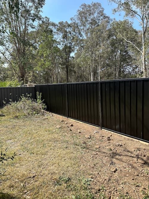 A Black Fence Is Surrounded By Trees In A Yard — Mid Coast Boundary Fencing In Old Bar, NSW