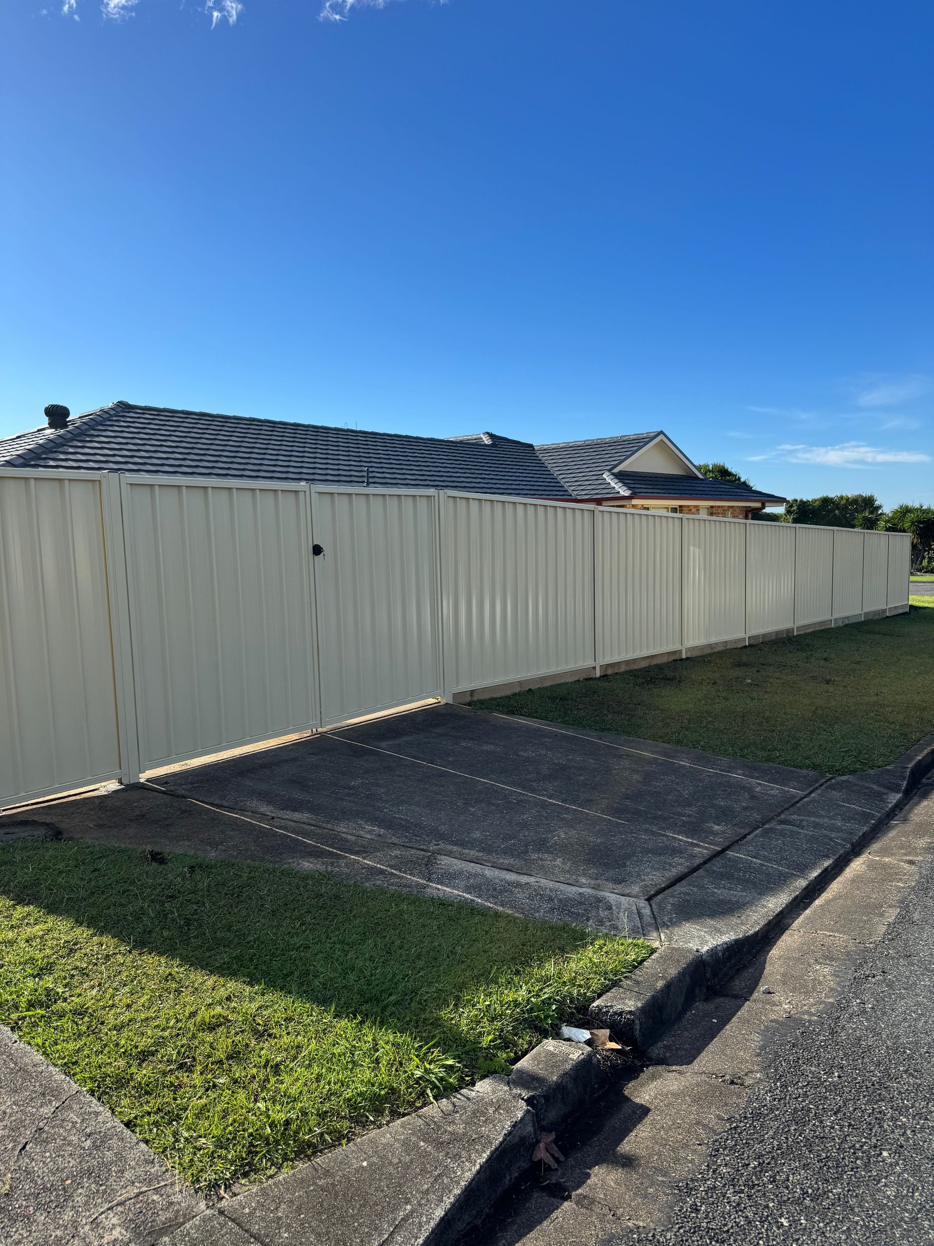 A Beige Fence Is Sitting In The Grass In Front Of A House — Mid Coast Boundary Fencing In Old Bar, NSW