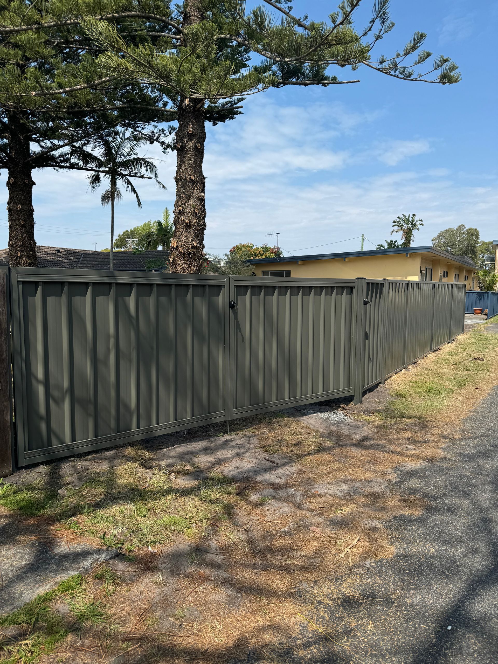 A Green Fence Surrounds A Grassy Yard In Front Of A House — Mid Coast Boundary Fencing In Old Bar, NSW