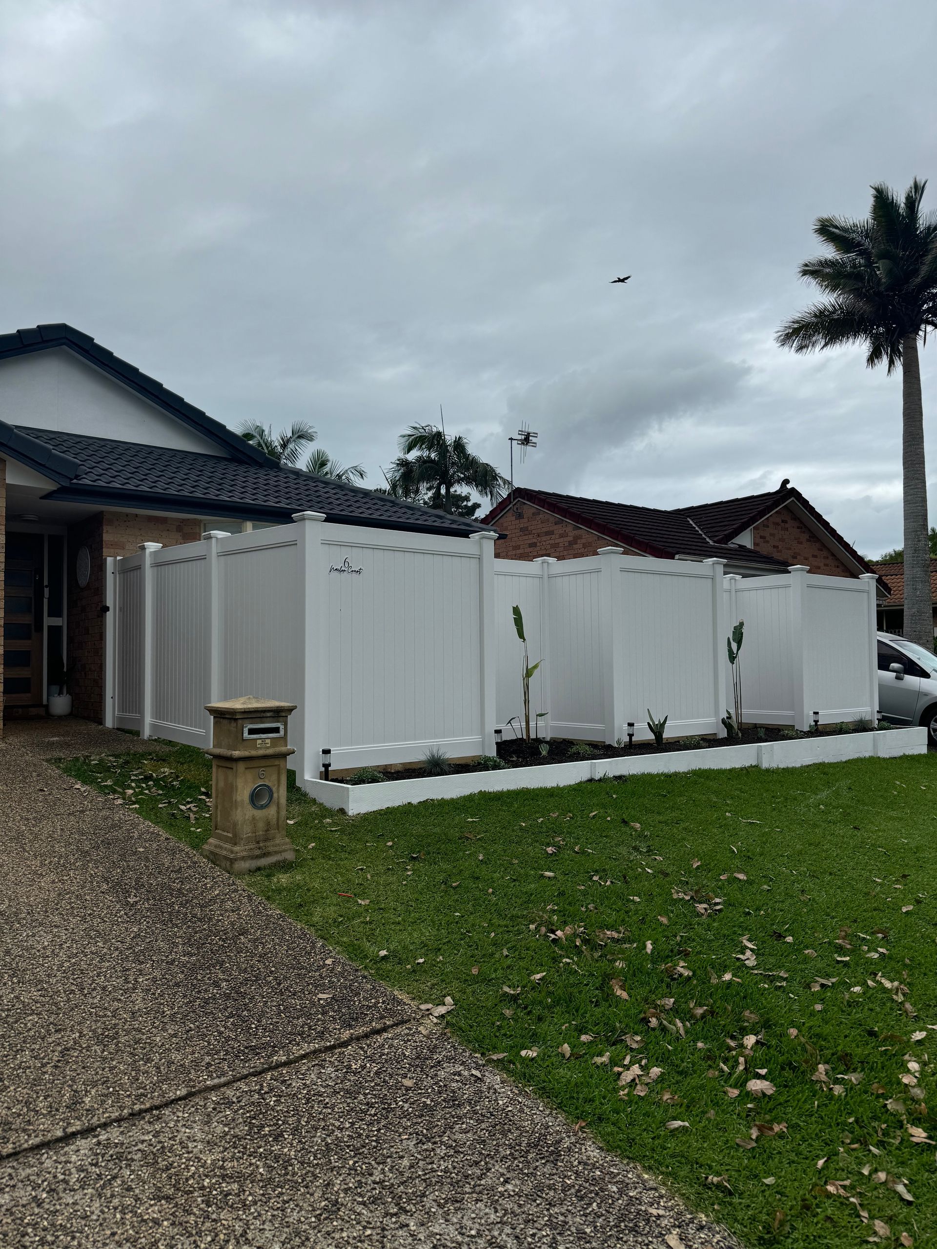 A White Fence Is Surrounding A House On A Sunny Day — Mid Coast Boundary Fencing In Forster, NSW