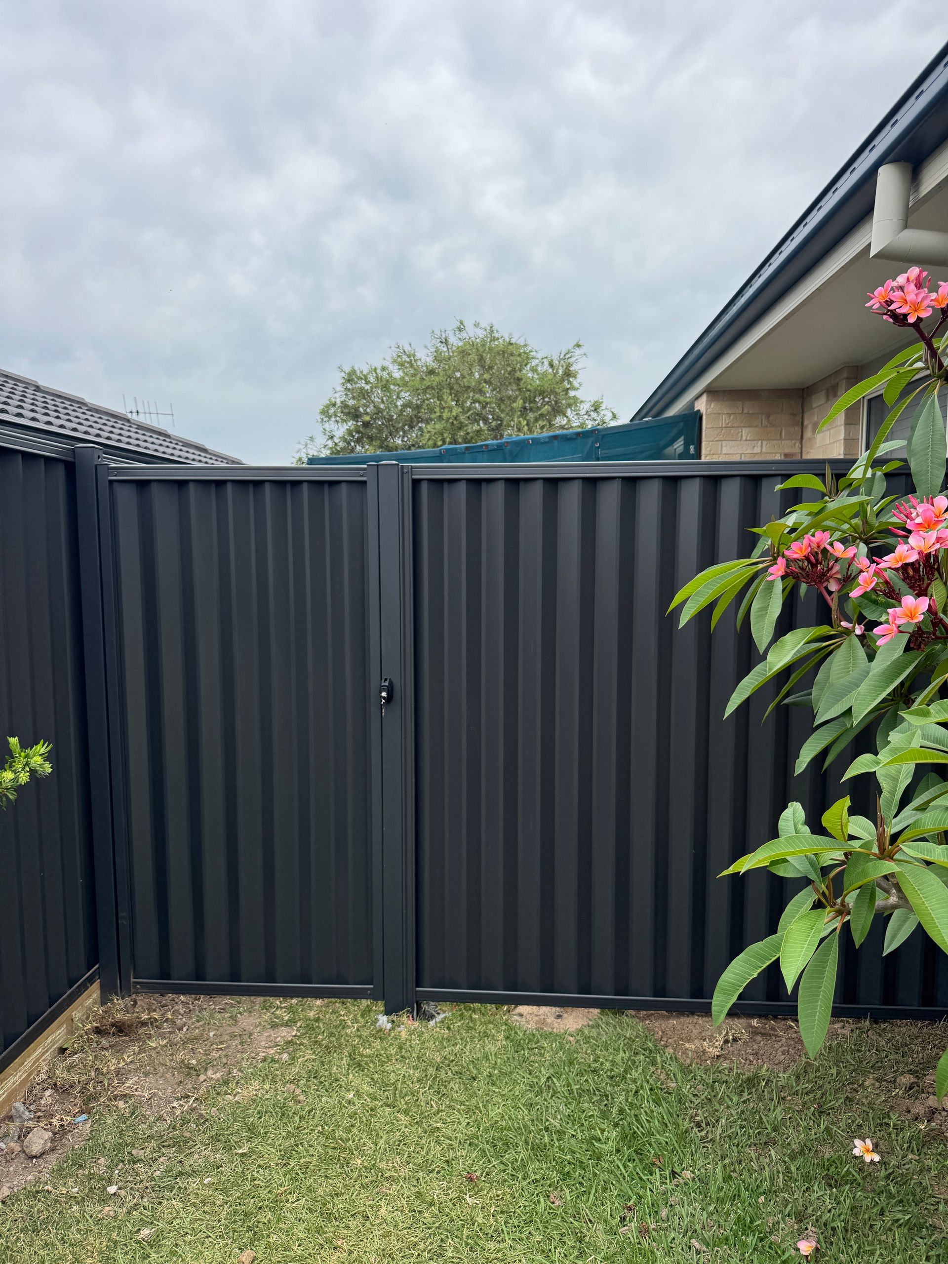 A White Fence Along The Side Of A Brick Building — Mid Coast Boundary Fencing In Old Bar, NSW