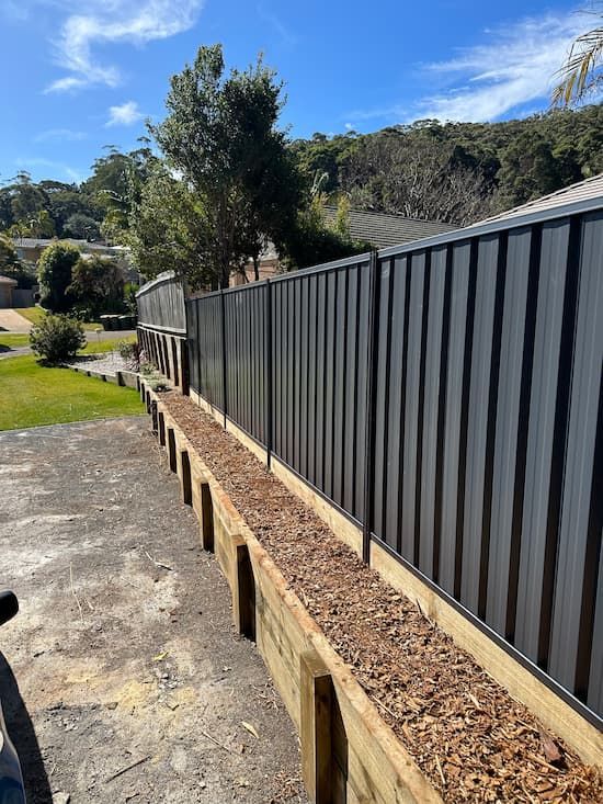 A Black Fence Is Surrounded By Wooden Beams And Gravel — Mid Coast Boundary Fencing In Old Bar, NSW