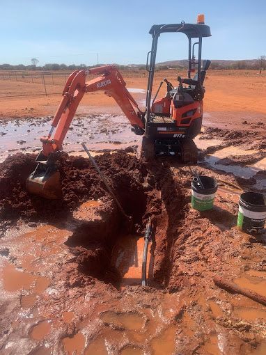 A Small Excavator Is Digging A Hole In The Dirt — Araluen Plumbing In Braitling, NT