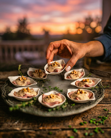 Una mano posiziona un antipasto a base di conchiglie su un piatto rustico al tramonto.