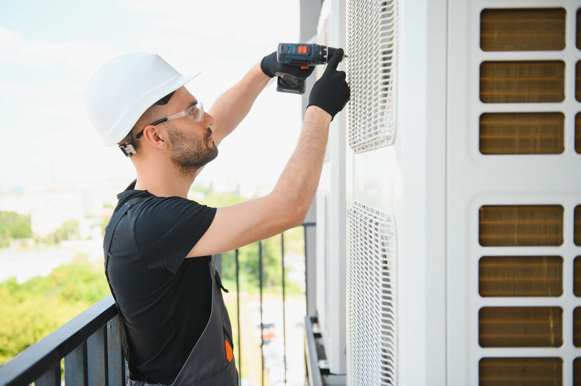 A man is using a drill to install an air conditioner on a balcony.