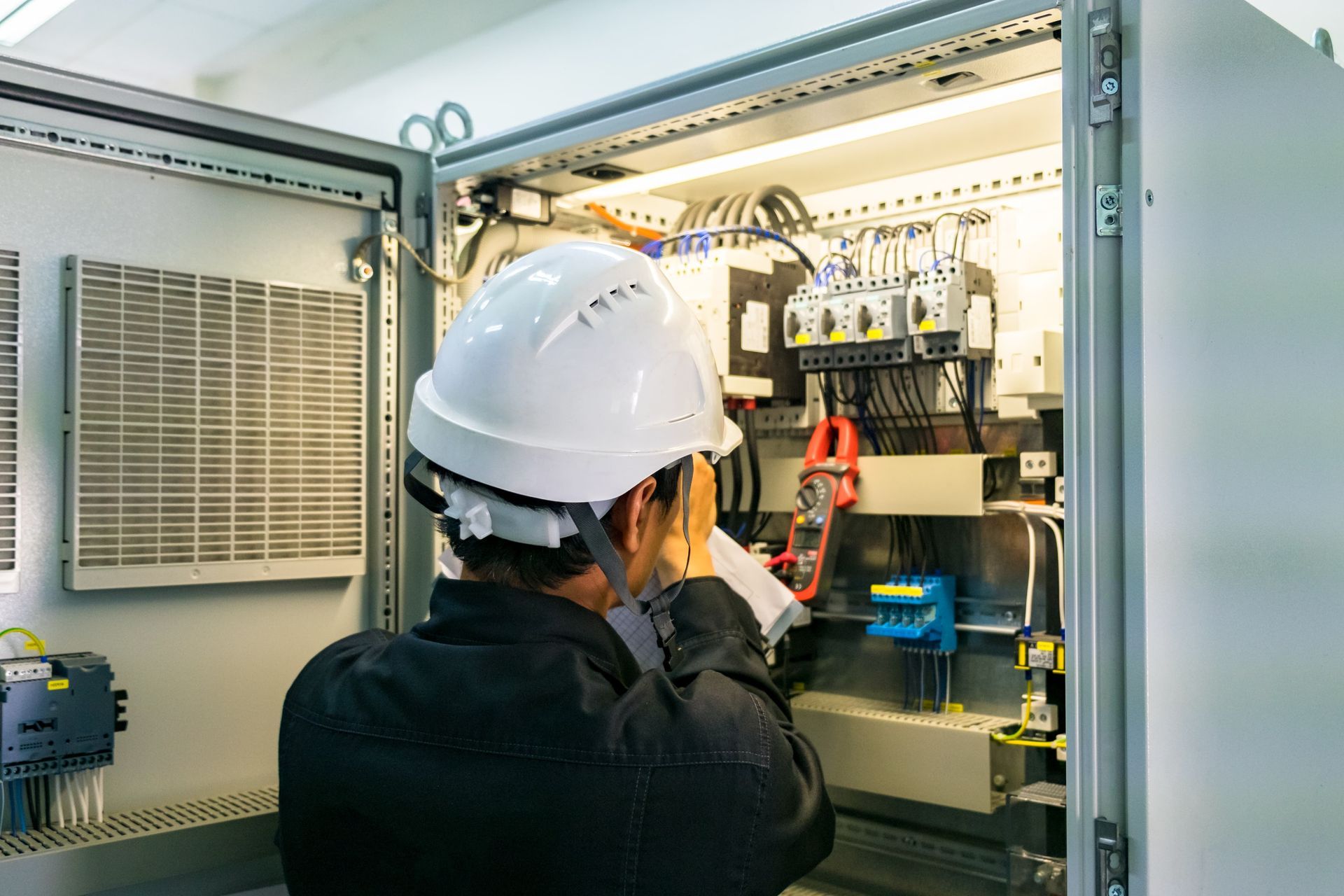 A man wearing a hard hat is working on an electrical box.