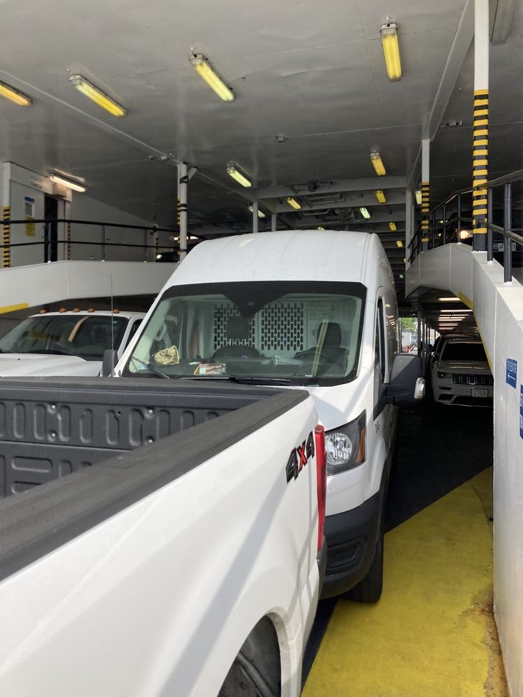 White van and pickup truck parked inside ferry, yellow and black striped support columns.