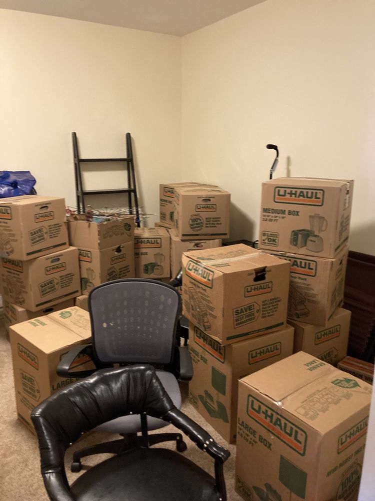 Room with many stacked U-Haul moving boxes, a black office chair, and a small ladder.