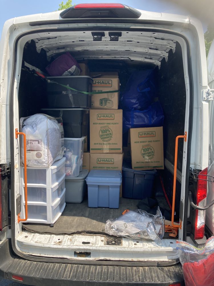 Back of a white van filled with moving boxes, bins, and other items.