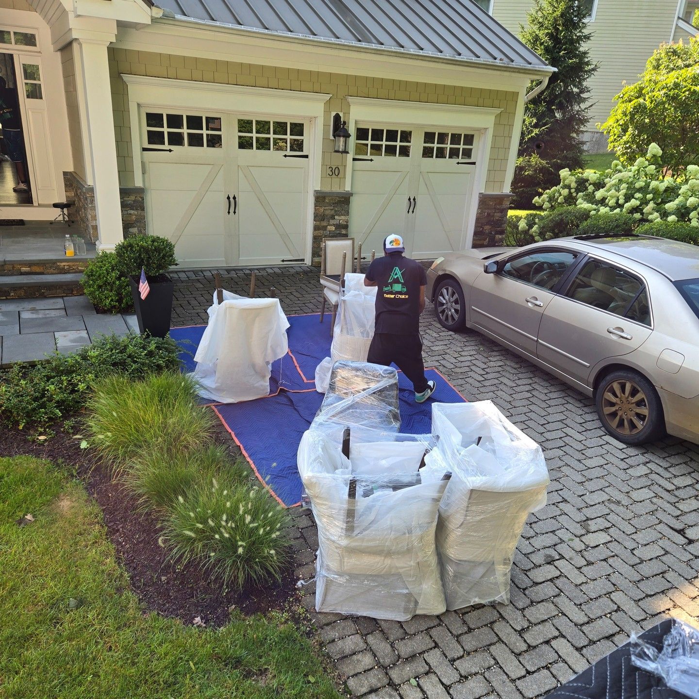 Moving crew loading wrapped furniture onto a truck in front of a house with a car parked nearby.