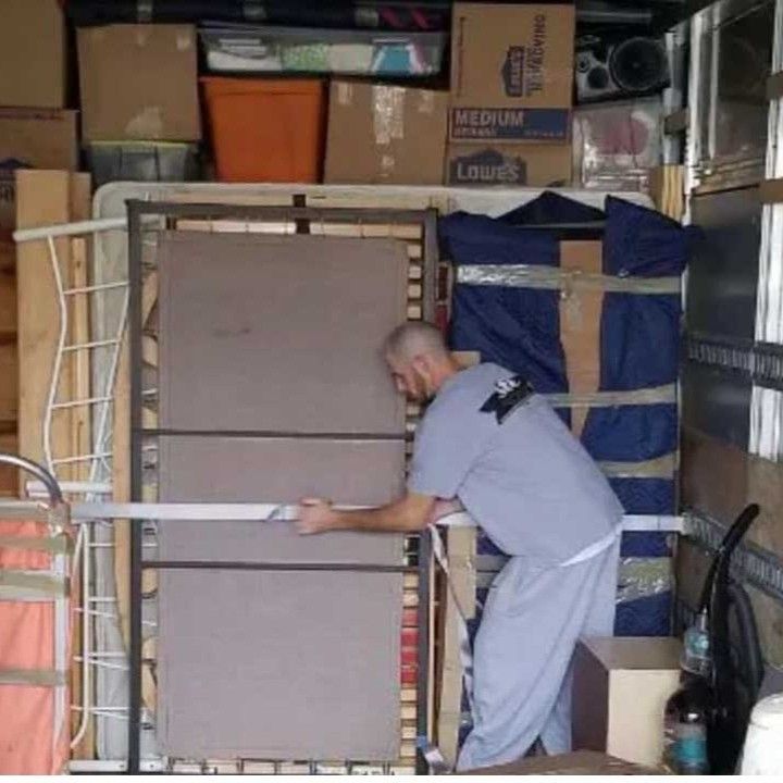 Man loading a box truck, holding a frame; boxes and furniture are packed inside.