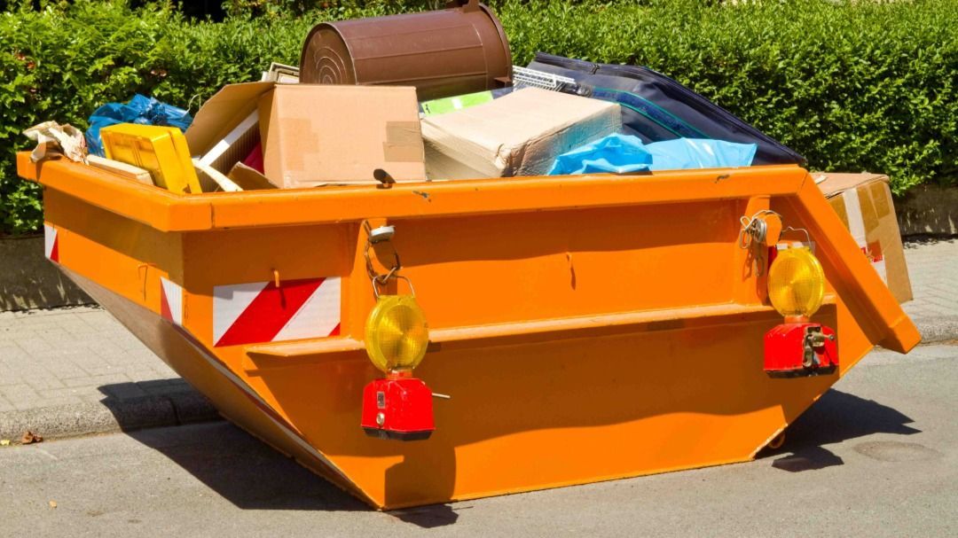 Orange dumpster filled with trash on a street, with reflectors.