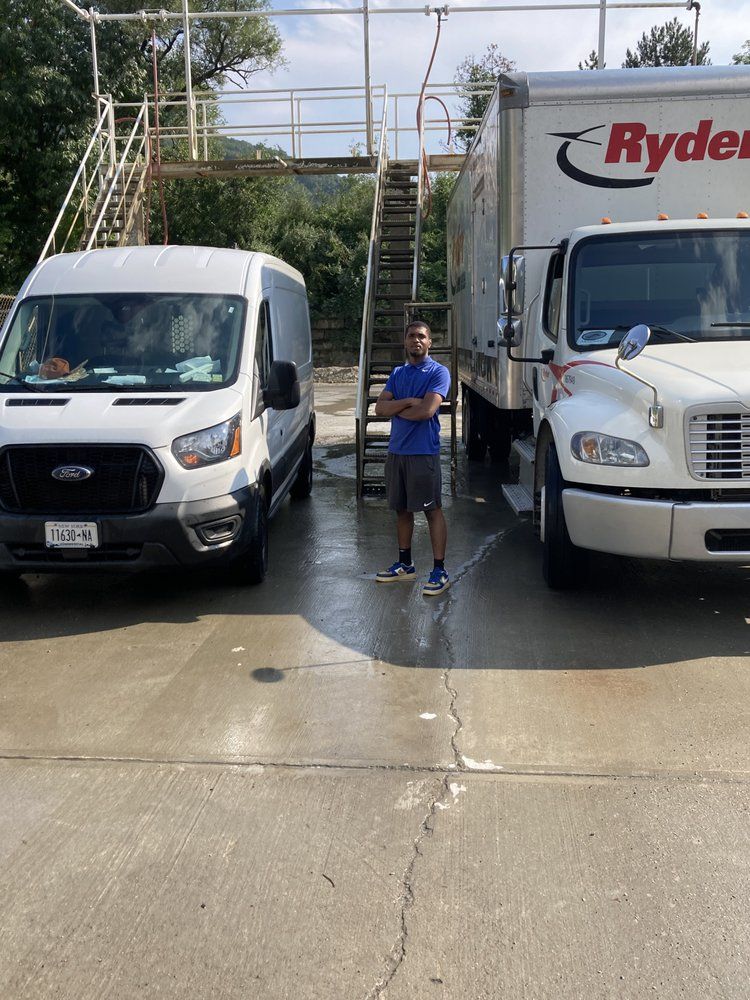 Man standing between a white van and a Ryder truck; near outdoor metal stairs, sunny day.