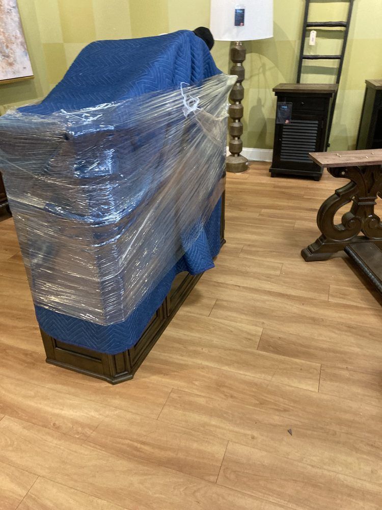 Furniture wrapped in blue padding and plastic, on a wood floor in a showroom.