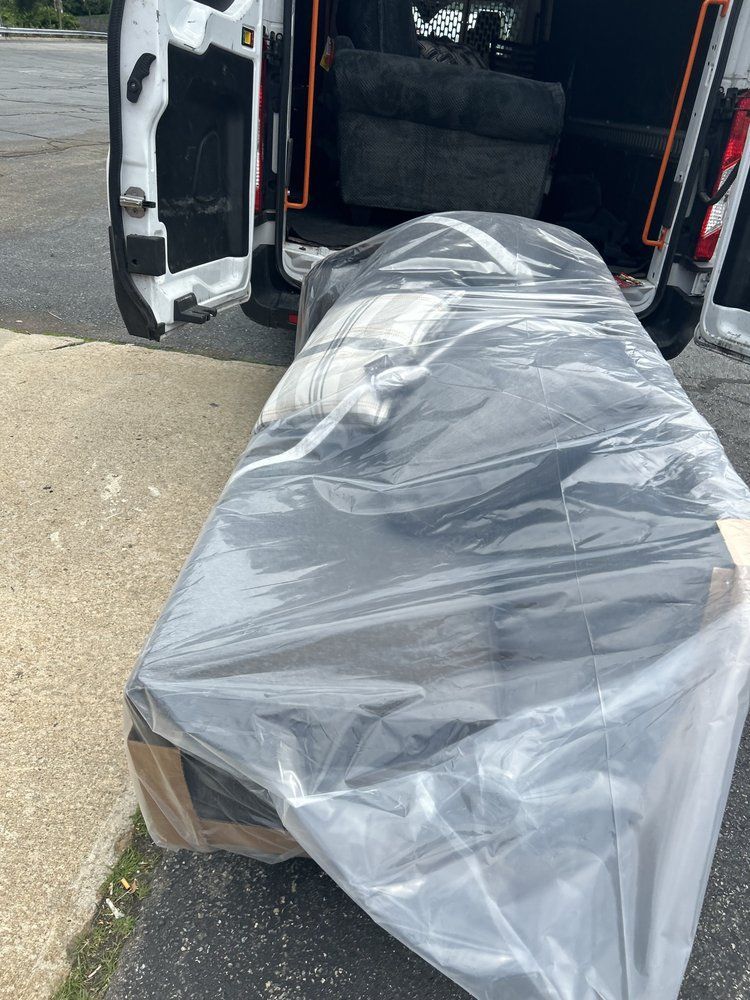 A sofa wrapped in plastic is being loaded into a white cargo van.