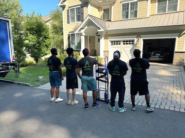 Five movers standing in front of a house, looking at a parked moving truck.