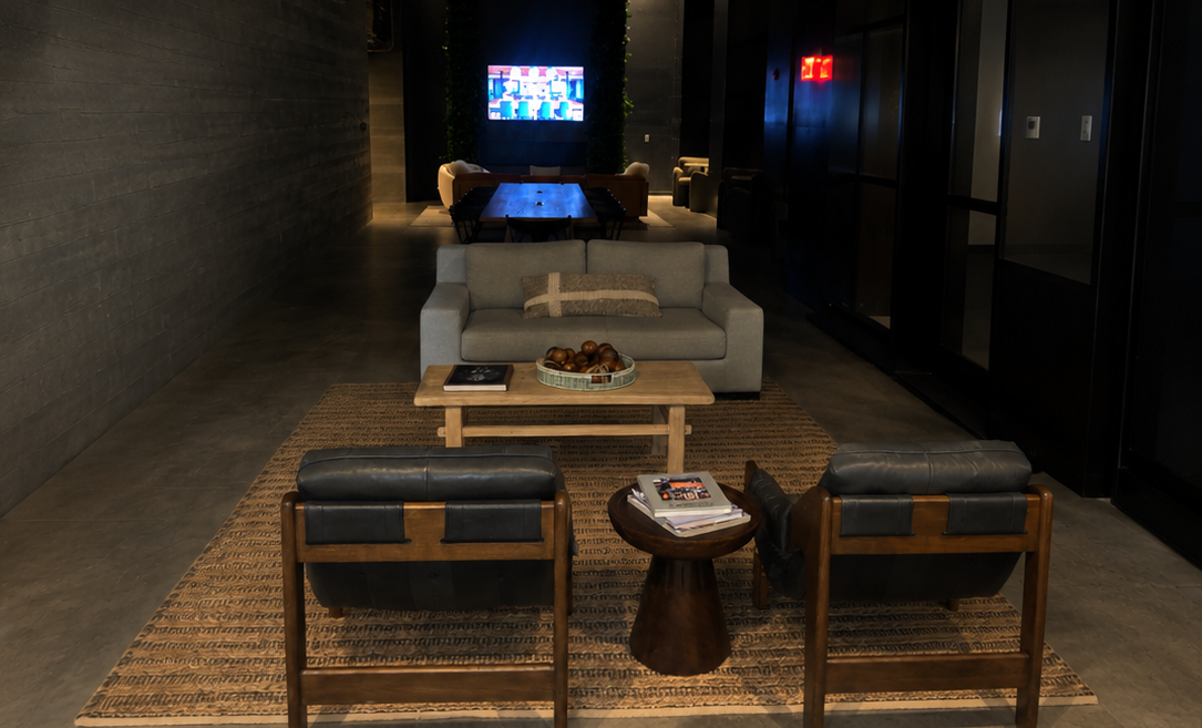 Modern lounge with sofas, armchairs, low tables, and a TV at the far end of a dark hallway.