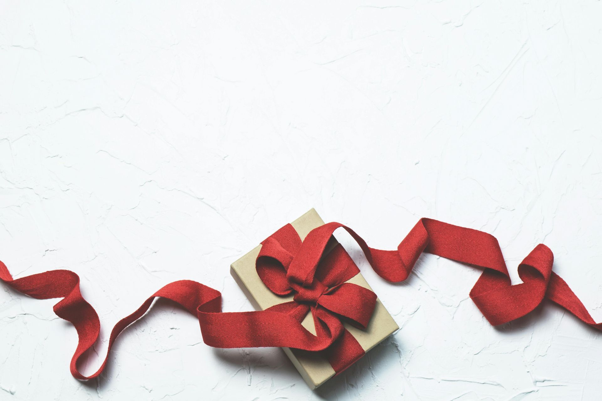 Gift box with red ribbon on white textured background.