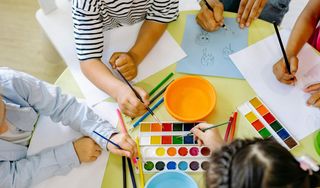 Children seated around an art table, painting and making art