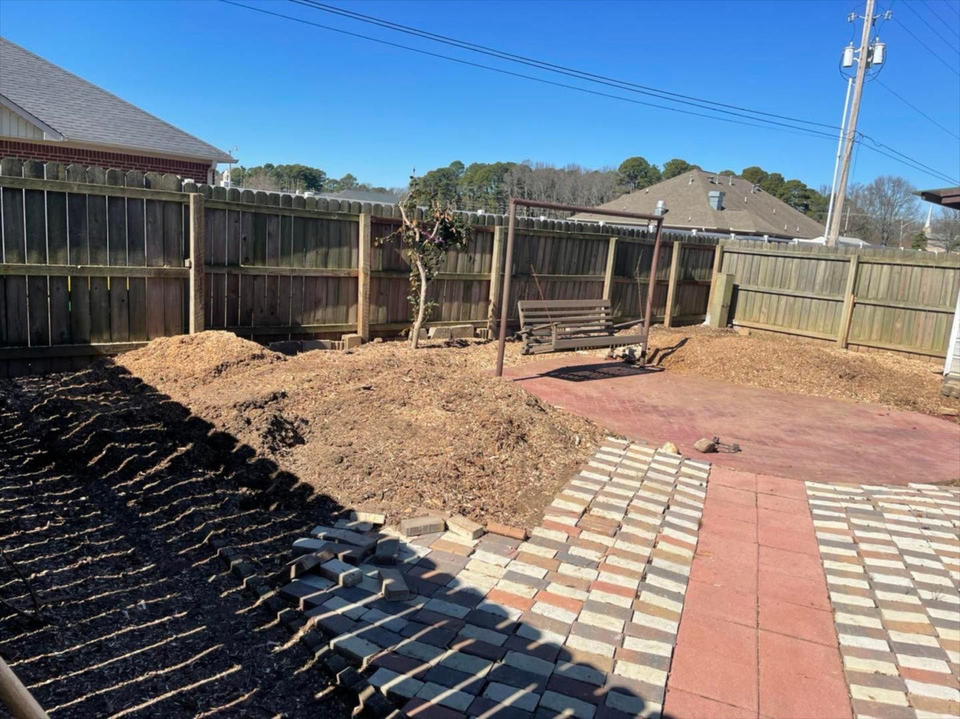 A backyard with a wooden fence and a brick walkway.