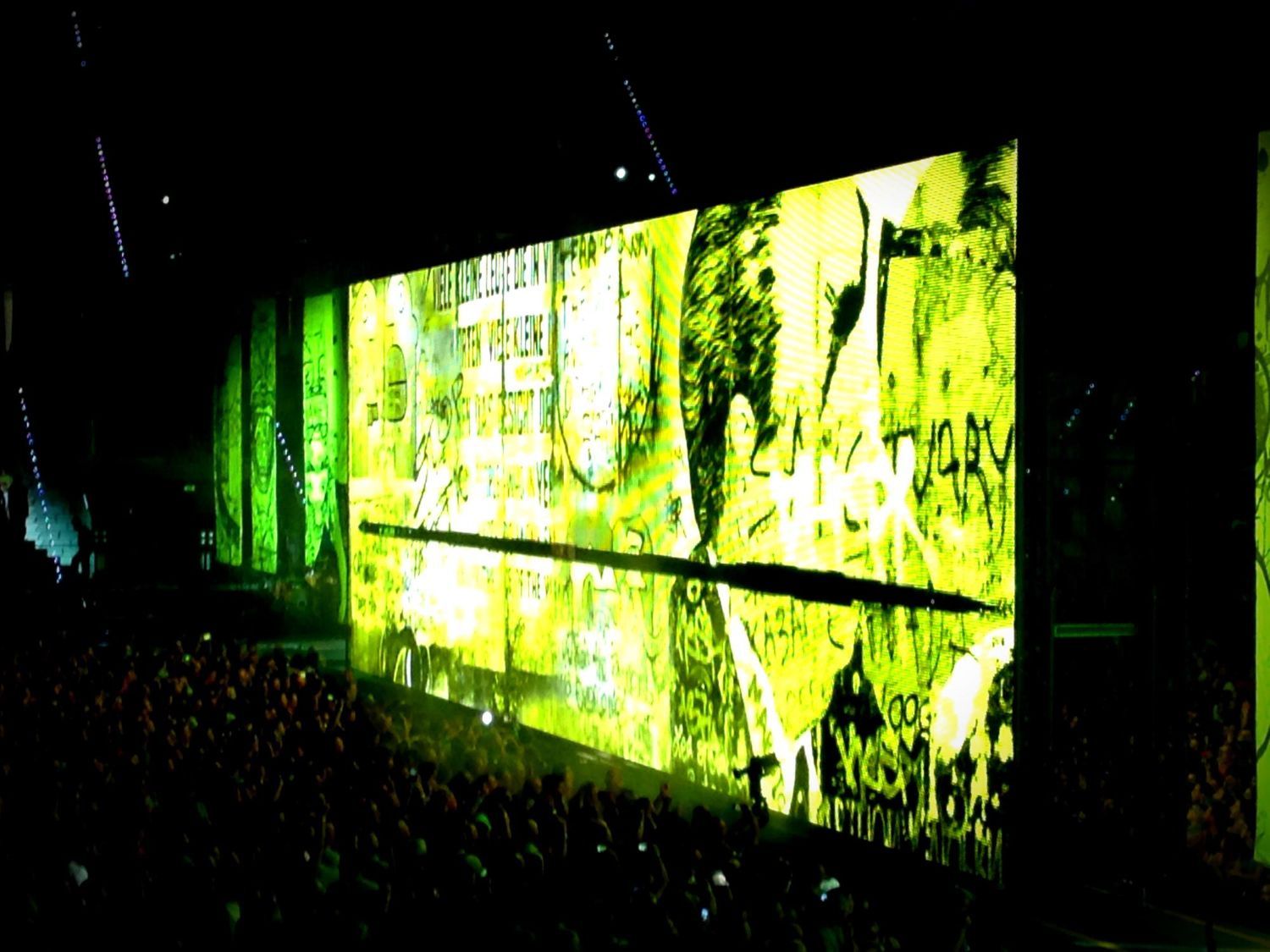 Una multitud de personas viendo un concierto con una gran pantalla detrás que dice victoria