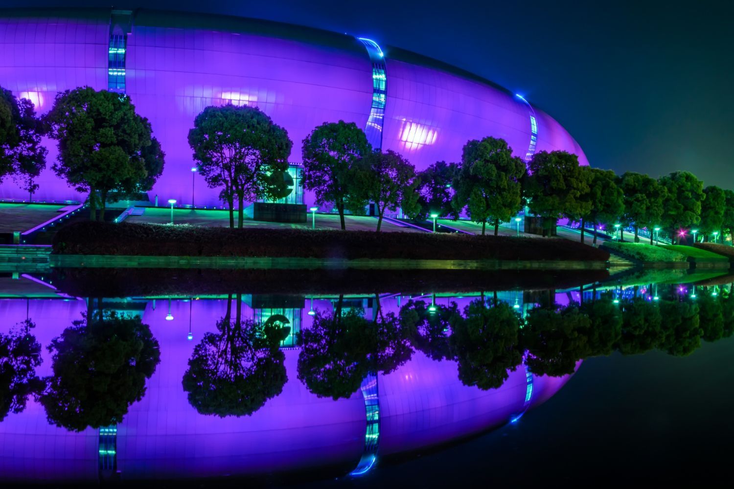 Un edificio con luces violetas se refleja en el agua.
