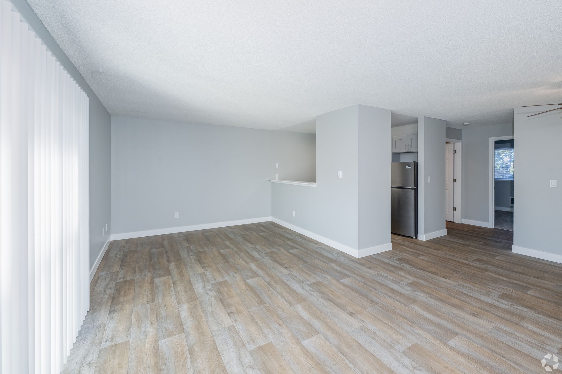 An empty living room with light gray walls, wood-look flooring, and an open entryway to a kitchen.