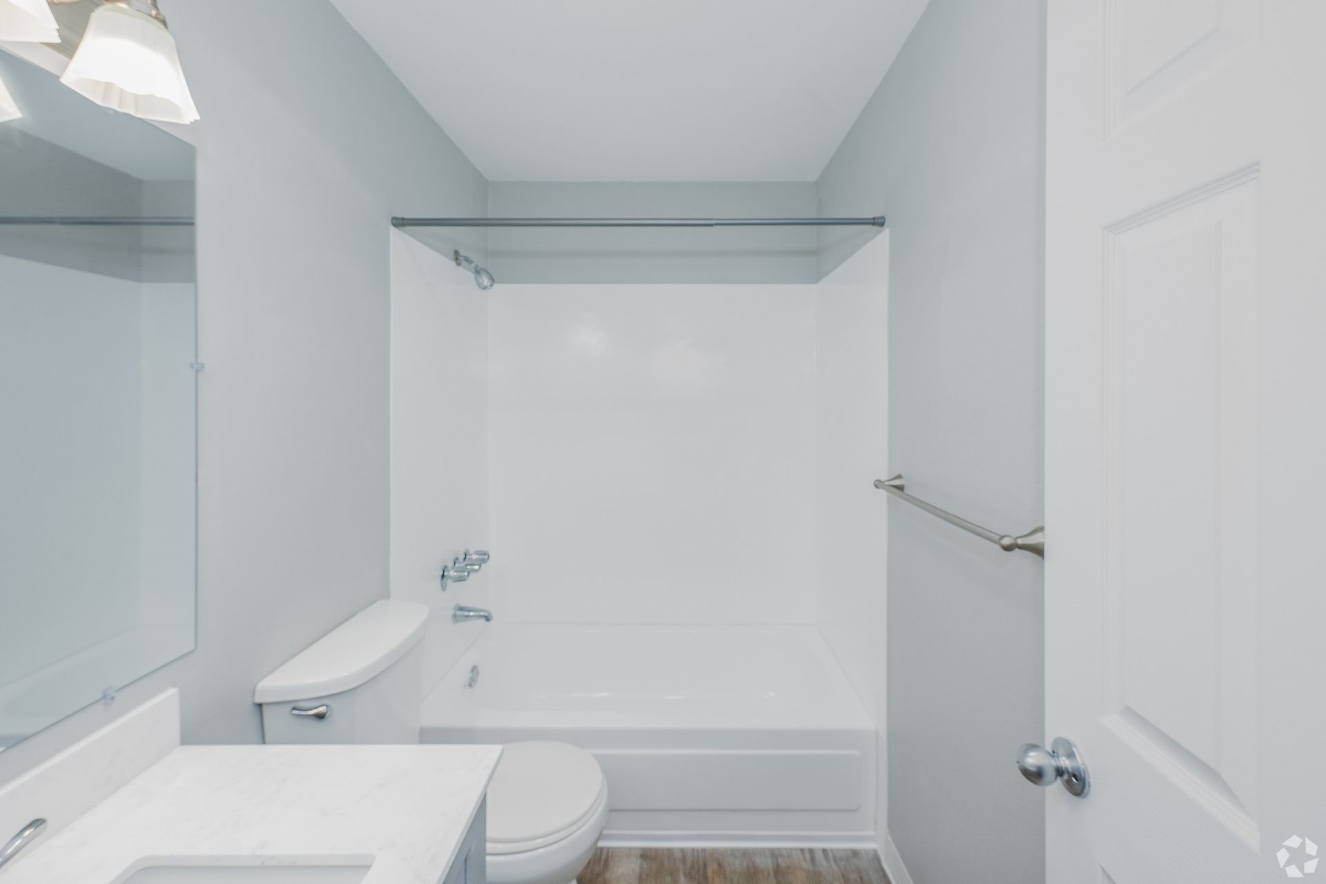 A modern bathroom featuring a white vanity with a mirror, a toilet, and a white bathtub with a silver shower rod.