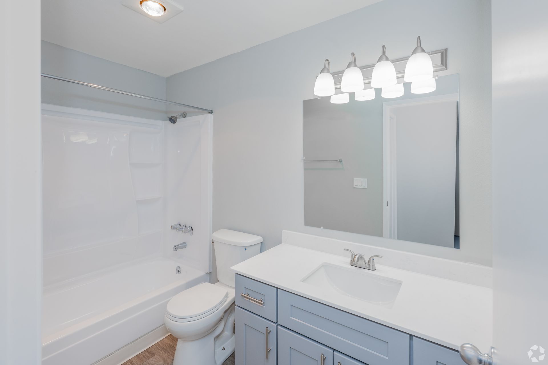 A modern bathroom with light gray walls, a white vanity with a rectangular mirror, and a shower-tub combination.
