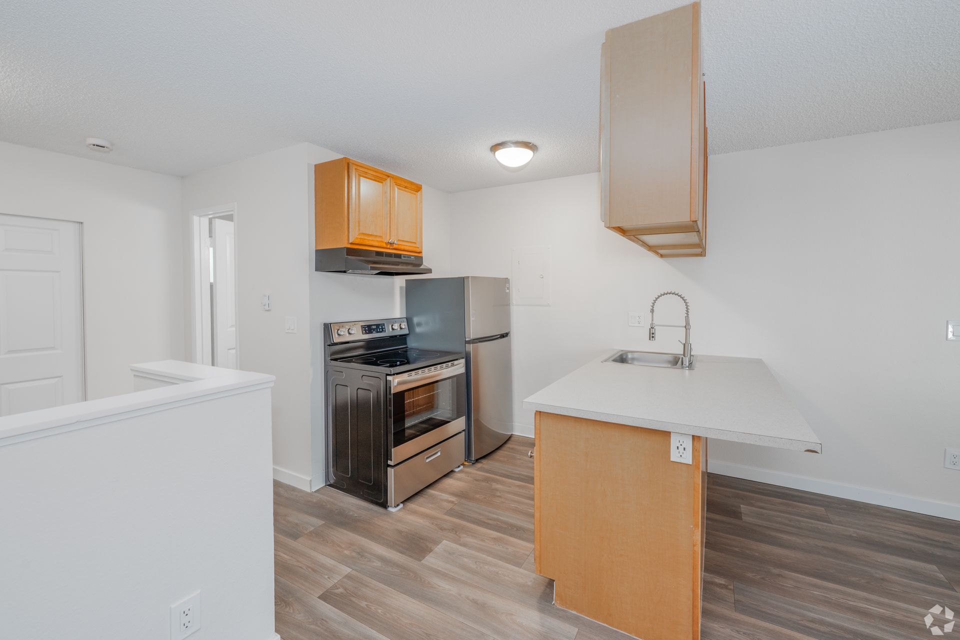 A modern kitchen featuring a stainless steel stove, refrigerator, wood-finish cabinets, and a white countertop island.
