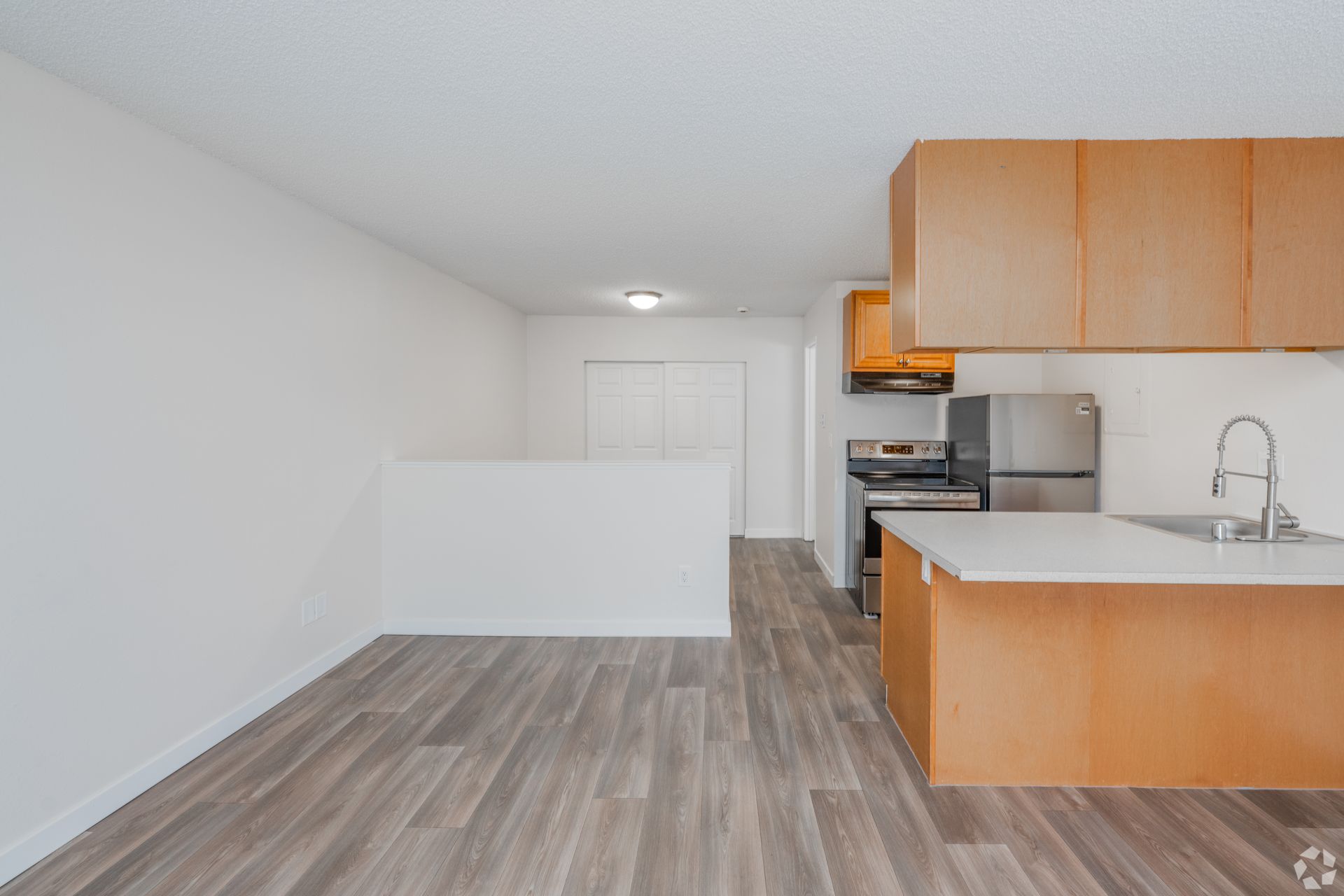 A kitchen with wood-toned cabinets, light-colored countertops, stainless steel appliances, and wood-look flooring.