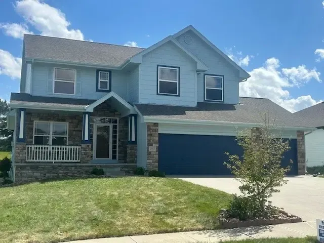Blue two-story house with stone accents, a two-car garage, and a green lawn under a blue sky.