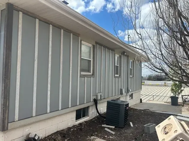Gray and white exterior of a house, vertical siding with windows, and an AC unit.