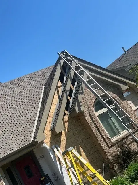 Ladder on a brick house roof with architectural details under a blue sky.