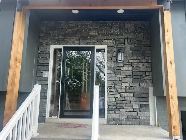 Entrance with stone wall, glass door, wooden beams, and white railing.