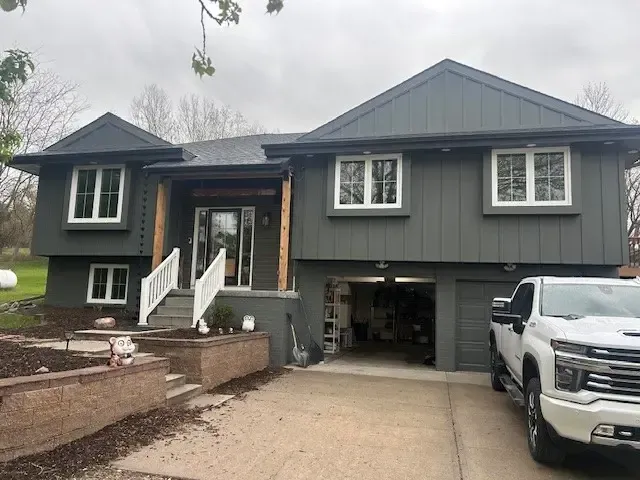 Dark gray house with white trim, garage, and truck in the driveway under a cloudy sky.