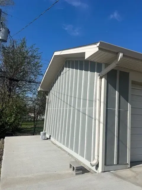 Gray and white sided building with concrete foundation under a blue sky.