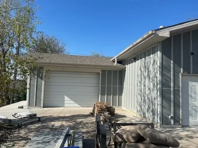 Exterior of a house with a garage and light blue siding; a blue sky overhead.