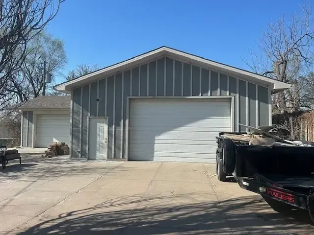 Gray garage building with white doors and a concrete driveway on a sunny day.