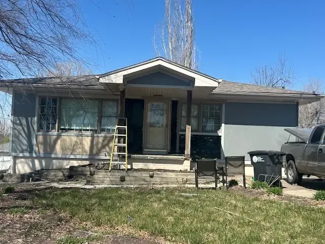 Rundown one-story house with gray siding, porch, and a truck parked outside.