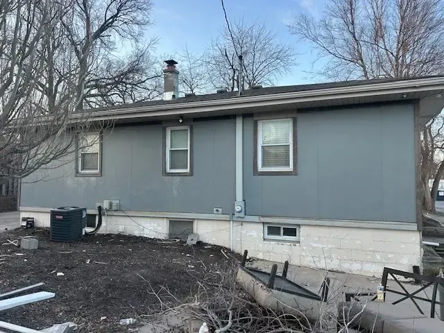 Gray house exterior with windows, chimney, and air conditioning unit. Overcast day.