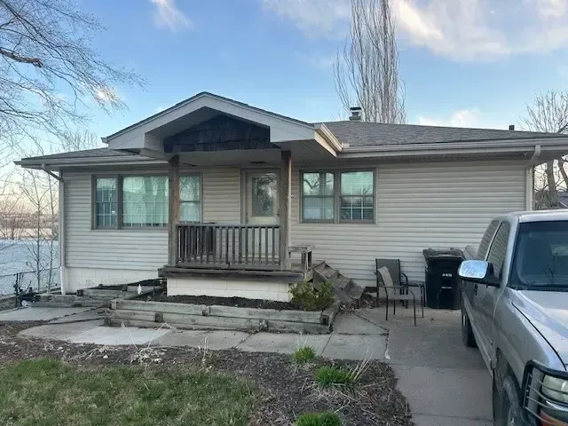 Beige house with porch, windows, and silver truck parked nearby on a sunny day.