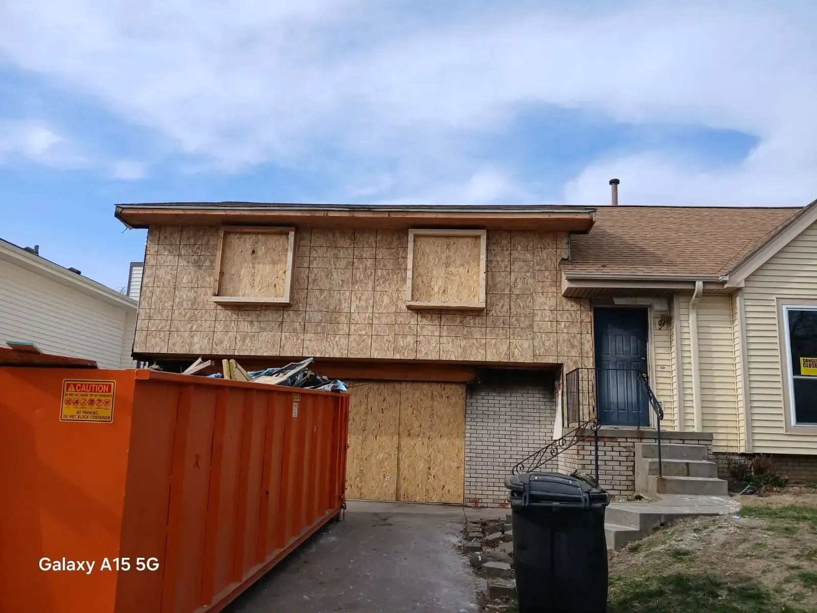 House under construction with boarded-up windows and an orange dumpster in the driveway.