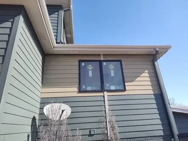 Exterior of a house with two-tone siding, windows, and a satellite dish against a blue sky.