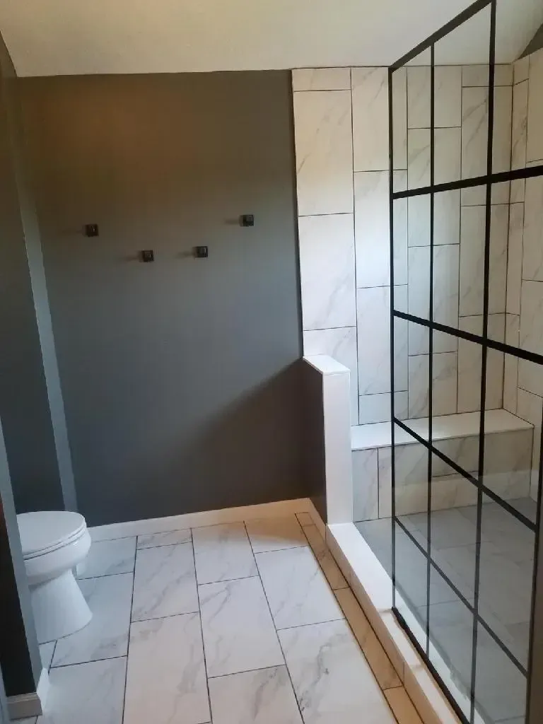 Modern bathroom with grey walls, white marble tile, and a black-framed glass shower.