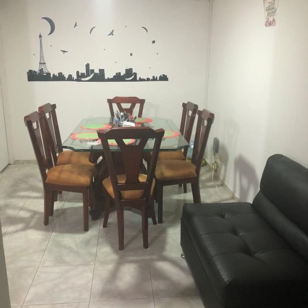 Comedor con mesa de cristal, seis sillas de madera y un sofá negro. Arte decorativo de pared.