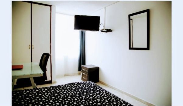 Dormitorio con cama, escritorio, TV, armario y espejo sobre paredes blancas.