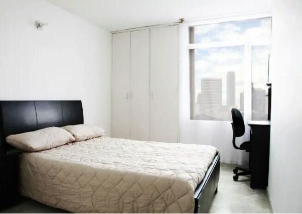 Dormitorio con cama negra, armario blanco, escritorio y ventana con vista al horizonte de la ciudad.