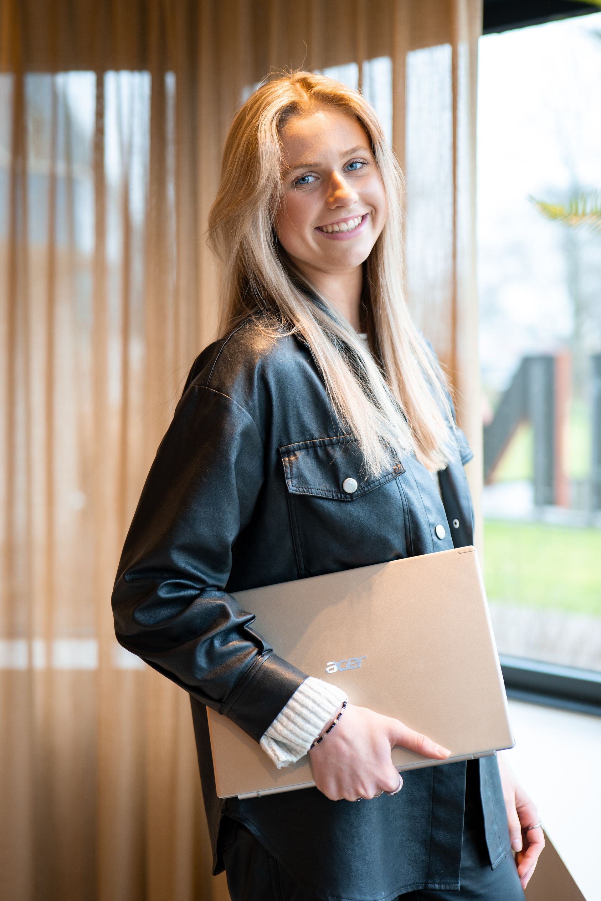 Een vrouw in een zwart leren jack houdt een laptop vast.