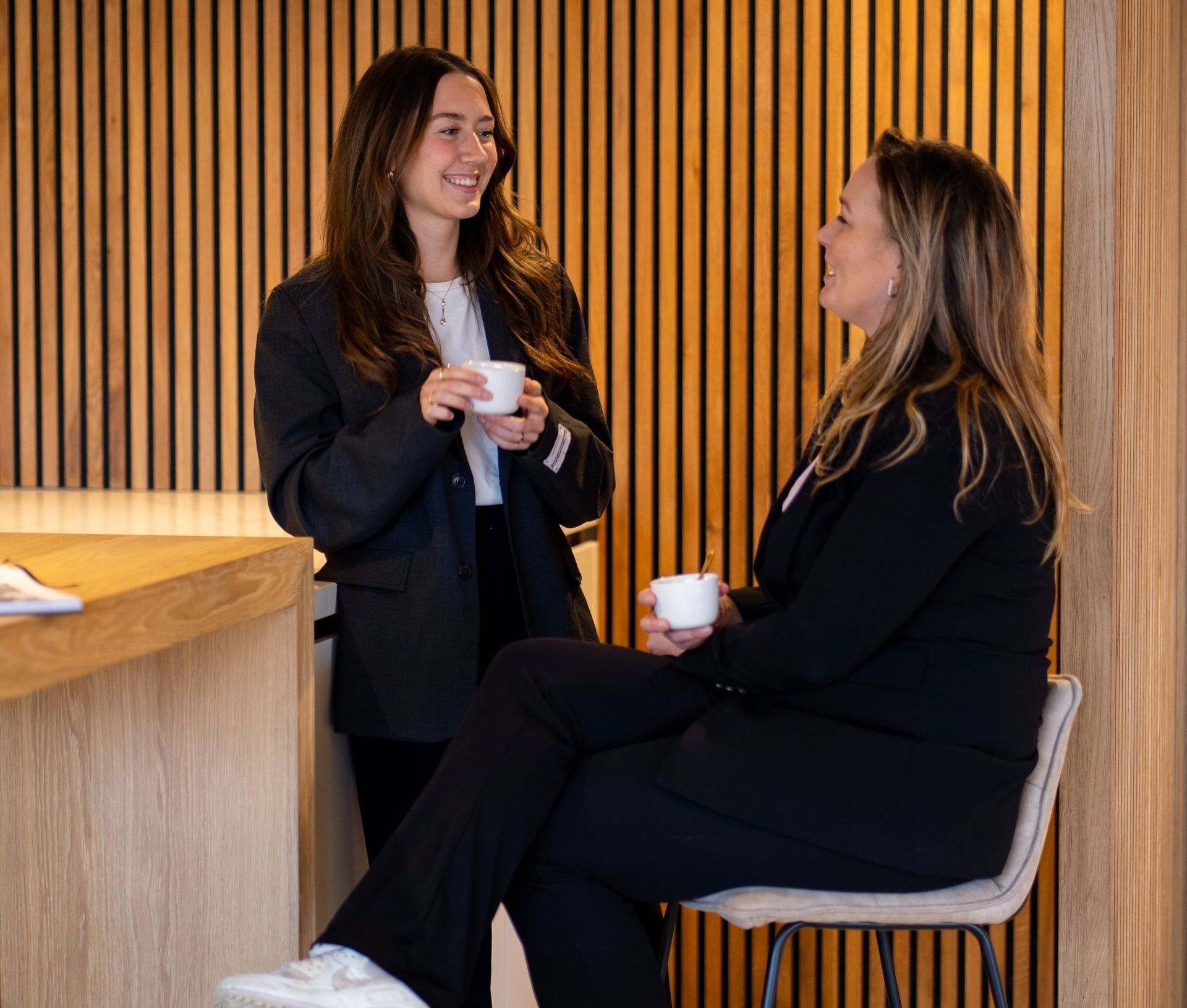 Twee vrouwen praten met elkaar terwijl ze kopjes koffie vasthouden.